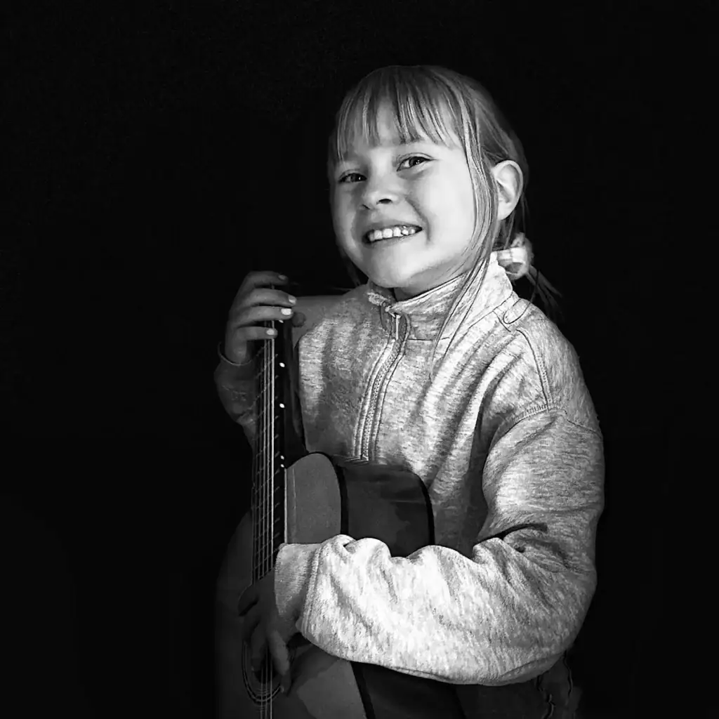 Young girl smiling with guitar, focused on music, Pudsey Camera Club.