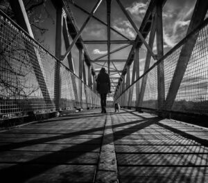 Person walking on a bridge with a dog, black and white photo.