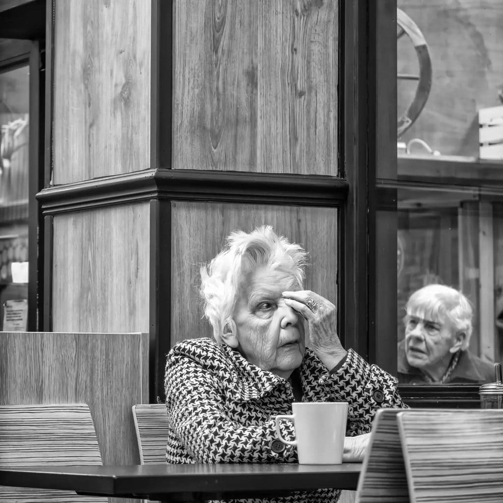 Pudsey Camera Club Member Image Elderly woman with white hair wiping her eye in a cafe setting.
