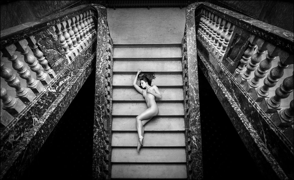 Nude figure on a grand staircase with ornate railings, Pudsey Camera Club at the end.